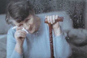 Lonely senior woman with walking cane crying in the window.