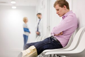 Man looking at brace on knee while sitting in hospital waiting room.