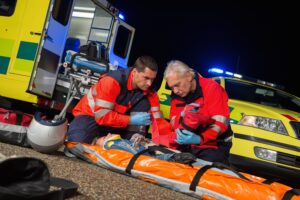 Paramedics giving first-aid to injured motorbike woman driver at night.