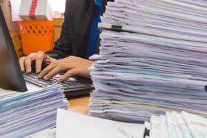 Man working in his desk loaded with stack of paperwork.